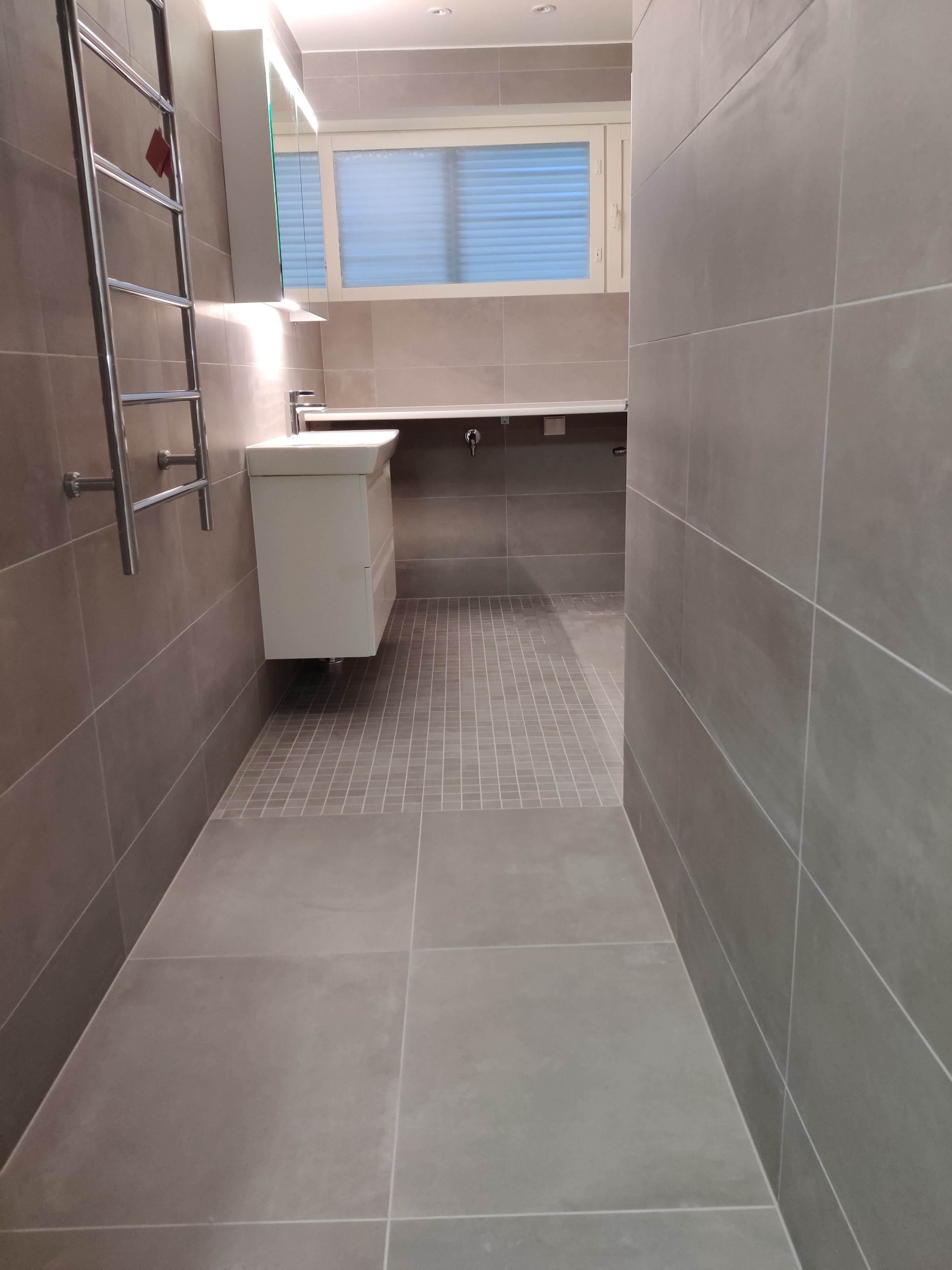 A renovated bathroom with a walk-in shower and full-height tiling, completed by Pohjola Constructions